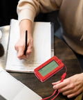 Woman writing with a red Transparent Mini Lucky Number Picker For Parties on a table with a clear display next to a laptop