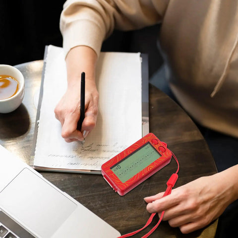 Woman writing with a red Transparent Mini Lucky Number Picker For Parties on a table with a clear display next to a laptop