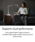 Woman reading with Solarcycle Morph Desk Light With Adaptive Daylight Tracking, sleek lamp on table, enhancing visual performance.
