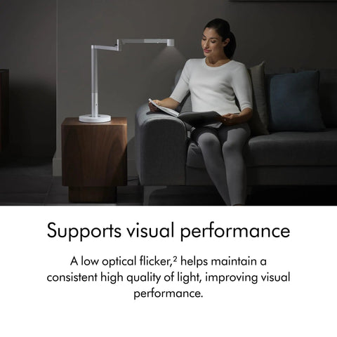 Woman reading with Solarcycle Morph Desk Light With Adaptive Daylight Tracking, sleek lamp on table, enhancing visual performance.