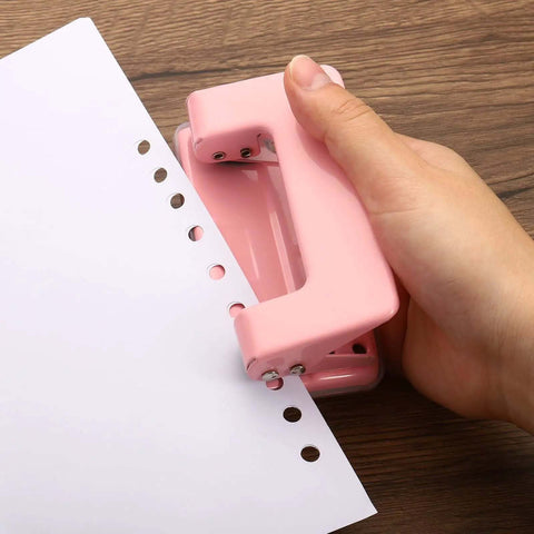 Hand holding pink paper puncher creating clean holes in sheet, showcasing durable design and ease of use for home and office.