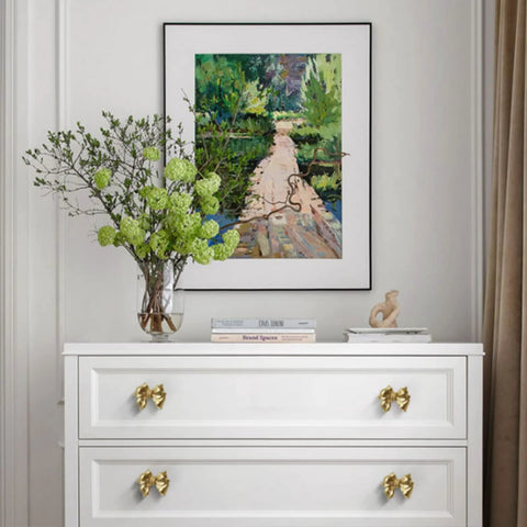 Gold Bow Cabinet Knobs Set Two Pack Brass Finish Bow Shaped Pulls on white dresser drawers in a room with framed artwork.