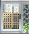 View through a white-framed window showing a cityscape with high-rise buildings and a potted plant on the windowsill.