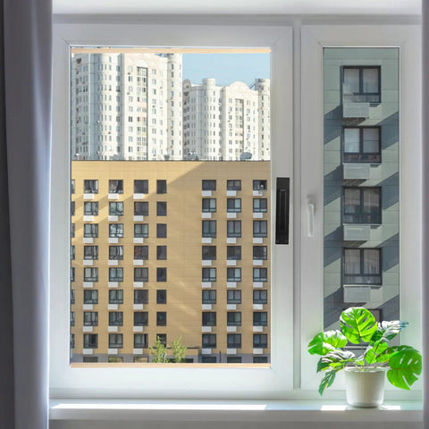 View through a white-framed window showing a cityscape with high-rise buildings and a potted plant on the windowsill.
