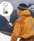 Hiker holding a sturdy outdoor compass keychain for backpacking and travel, pocket size navigation gadget for hiking in snowy mountains.