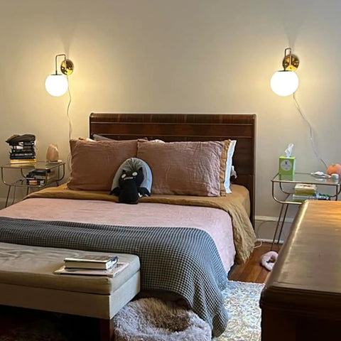 Bedroom with brass swing arm wall light fixture featuring gold plug in wall sconce with milk glass shade on either side of bed