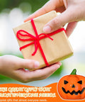 Person handing a wrapped gift with a red ribbon, featuring Top Notch Halloween Bathroom Glow Up Dope Ghost Pumpkin Toilet Seat Bolt Cover Cap Set.