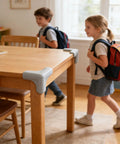 Table with Three-Sided Wrap Table Corner Protectors, No-Drill PVC Self-Adhesive Guards for Tables in a room with children walking by.