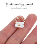 Close-up of a white miniature purse with gold chain from the Three Pack Mini Handbag Set For Dollhouse Decor And DIY Jewelry Charms.