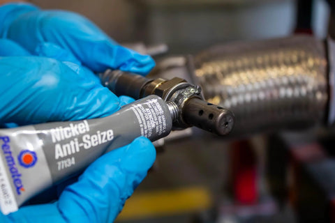 Permatex Nickel Anti-Seize lubricant tube, 0.5 oz, held by blue-gloved hand near a metal threaded component.