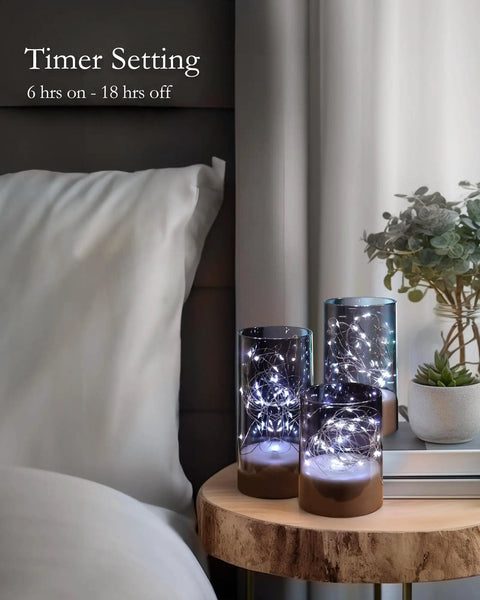 Set Of 3 Flameless Candles In Gray Glass Cylinders With Remote For A Cozy Vibe on nightstand with plant, ambient lighting