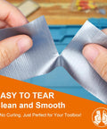 Hands gripping and tearing a roll of Silver Duct Tape, showcasing ease of use with clean tear in a toolbox context.