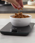 Digital Glass Top Kitchen Scale With 11 Lb Capacity in use, measuring dry ingredients in a white bowl, black finish, countertop setup.