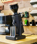 Dope Stepless Coffee Grinder Featuring 40mm Stainless Steel Conical Burrs For Pulling Consistent Espresso Shots And Brewing Smooth Daily Drips With Hella Low Retention In Matte Black on a wooden table.