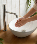 Person washing hands in NUESTRA VIDA Overhead Sink Oval Ceramic 16.1 * 13 * 5.5 IN, modern basin on wooden countertop.