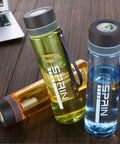 Colorful transparent water bottles with SPRIN logo on wooden table near laptop.