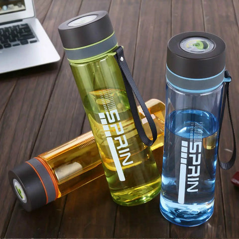 Colorful transparent water bottles with SPRIN logo on wooden table near laptop.