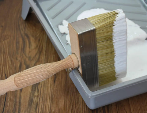 5.5 Inch Limewash Deck Brush With Wood Handle Large Paint Applicator resting in paint tray on wooden floor