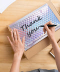 Person writing on Dope Metallic Bubble Mailers Set, 50 Self Seal Padded Envelopes, perfect for mailing; 7.3x5.1 inches shown