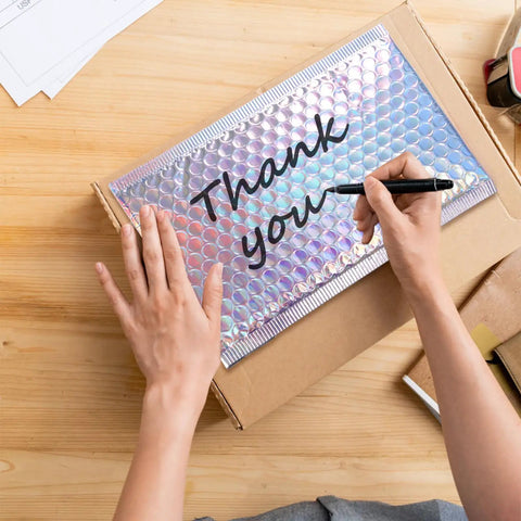 Person writing on Dope Metallic Bubble Mailers Set, 50 Self Seal Padded Envelopes, perfect for mailing; 7.3x5.1 inches shown