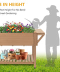 Mobile Raised Garden Bed With Lockable Wheels, Elevated Wood Planter With Storage Shelf And Protective Liner, Sturdy Outdoor Garden Box In Brown, filled with flowers and garden tools, next to silhouette of a gardener. 33-inch height for ease of use.