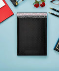 50 Pack Black PE Bubble Mailers With Self Seal Closure on desk, padded shipping envelopes for ecommerce and clothes shipping.