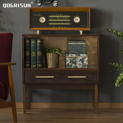 Vintage wooden cabinet with a retro radio on top, books, and decorative boxes in a mid-century modern styled room.