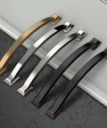 Set of five curved cabinet handles in different finishes, including brushed satin nickel, laid on a dark surface.