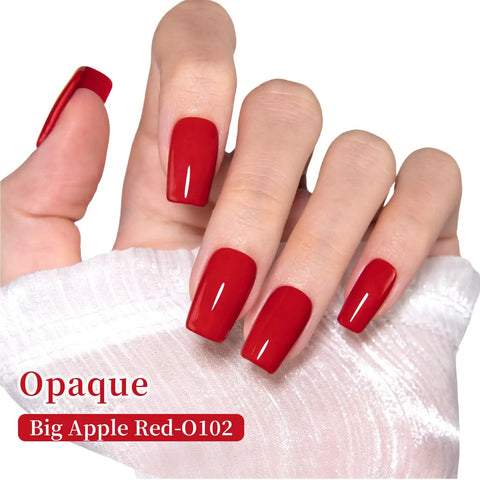 Hand with glossy nails painted Dope Big Apple Red Gel Polish Salon Grade 0.5 Fl Oz Soak Off UV LED Cure For 60 To 90 Seconds Safe Low Odor HEMA Free And TPO Free Nail Lacquer For Fall Winter Nail Art For Women And Girls against white fabric backdrop.