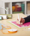 Front view of Cricut Basic Tool Set: 5-Piece precision craft tools used on pink vinyl with ribbon rolls on a craft desk