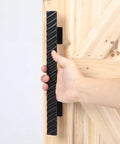 Hand holding solid brass sliding barn door handles set featuring 12 inch two sided design heavy duty mounting hardware installed