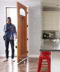 Heavy Duty Zinc Alloy Kickdown Door Stopper With Rubber Tip And Floor Grip Adjustable Drop Door Holder For No Slam Propping Open Doors In Silver Finish For Home And Office in use holding open a wooden door in a modern kitchen setting.