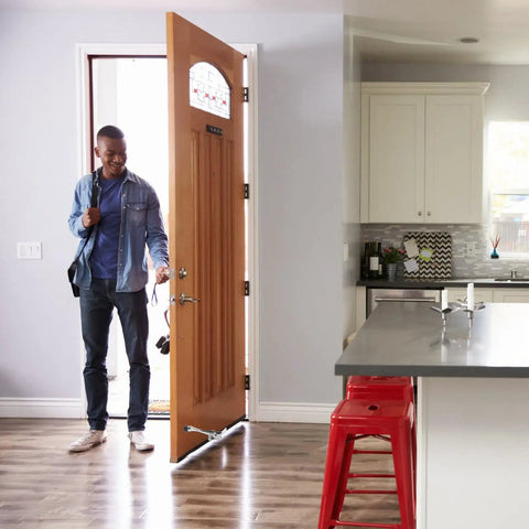 Heavy Duty Zinc Alloy Kickdown Door Stopper With Rubber Tip And Floor Grip Adjustable Drop Door Holder For No Slam Propping Open Doors In Silver Finish For Home And Office in use holding open a wooden door in a modern kitchen setting.