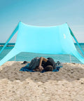 Couple resting under Portable Beach Tent Sun Shelter 7x7ft Shade Canopy UPF50 at a sandy beach, ocean in view.