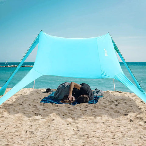 Couple resting under Portable Beach Tent Sun Shelter 7x7ft Shade Canopy UPF50 at a sandy beach, ocean in view.