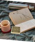 Open book and cup next to Small 10cm Alloy Feng Shui Compass With Flip Cover, Waterproof Outdoor Navigation Tool for camping.