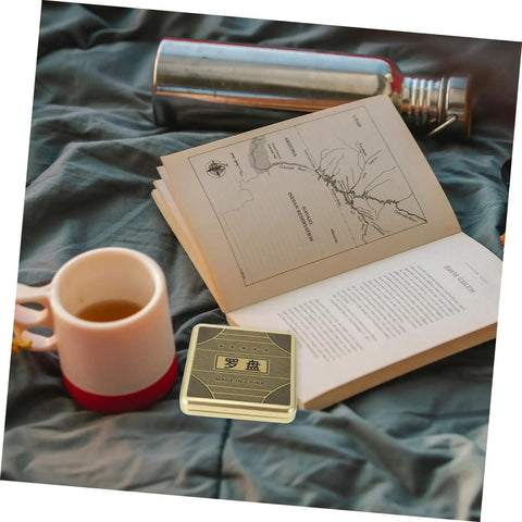 Open book and cup next to Small 10cm Alloy Feng Shui Compass With Flip Cover, Waterproof Outdoor Navigation Tool for camping.