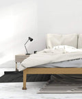 Minimalist bedroom with a wooden bed, bedside lamp, and decorative rugs on hardwood floor.