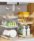 Total Game Changer Clear Three Tier Under Sink Organizer Two Pack with cleaning supplies and sponges in a cabinet.