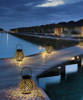 Outdoor Solar Lanterns Hanging Lights For Patio Porch Backyard Decorative Garden Lamps Metal Waterproof LED Lanterns With Auto On Off No Fuss Easy Setup Create Charming Shadow Patterns Two Pack illuminating a wooden boardwalk at night.