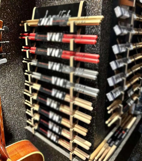 Wall Mounted Drum Stick Holder And Display Rack Heavy Duty Acrylic Organizer For Ten Pairs Of Drumsticks and Lightsabers Keeps Your Studio Rig Fresh Top Shelf Zero Clutter with red and natural drumsticks.