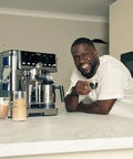 Person enjoying coffee beside Luxe Café Pro Series 4 In 1 Espresso Machine With Built In Grinder And Integrated Tamper