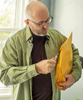 Yellow padded mailing envelope held by a bald man in glasses.
