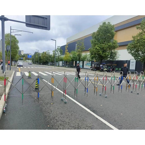 Heavy Duty Adjustable Stainless Steel Retractable Safety Gate Featuring Hella Smooth Moving Universal Casters And Rock Solid Brakes For Tight Garage And Store Layouts blocking a street with colorful casters.