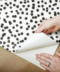 Hands peeling corner of Black and White Confetti Peel and Stick Wallpaper Removable Self-Adhesive Roll for Easy No Mess Decor