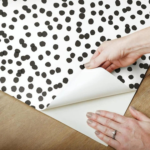 Hands peeling corner of Black and White Confetti Peel and Stick Wallpaper Removable Self-Adhesive Roll for Easy No Mess Decor