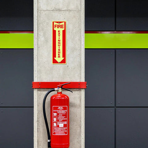 Heavy Duty Fire Extinguisher Signs 12 Pack Made From Rust Free Aluminum 12 By 4 Inch Glow In The Dark Waterproof Weatherproof Fade Resistant Two Pre Drilled Holes For Easy Indoor Outdoor Mounting installed on concrete wall above fire extinguisher.