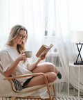 Woman sitting by a window with a book, next to a modern table lamp from the Set Of 2 Modern Table Lamps With 3 Way Dimmable Touch Control.