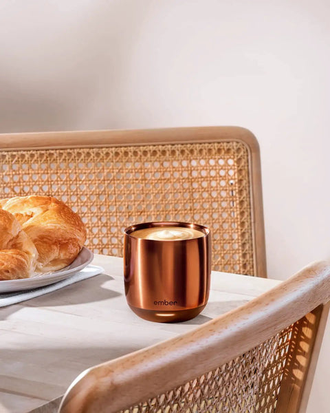 Renewed 6 Oz Smart Heated Coffee Mug With App Precision Temp Control and Solid Battery Life on a table beside a croissant.