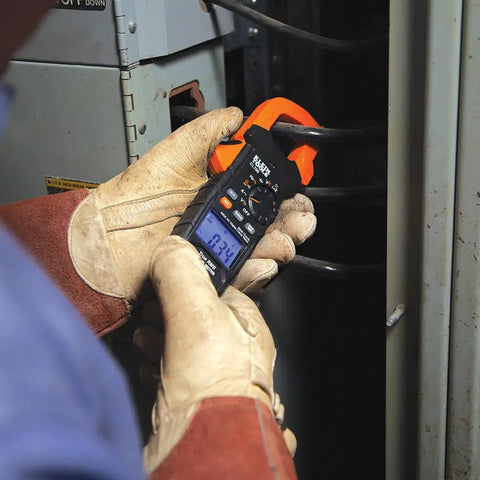Technician using Auto Ranging Digital Clamp Meter TRMS 600A for AC DC Voltage Current LoZ Mode in a panel box.
